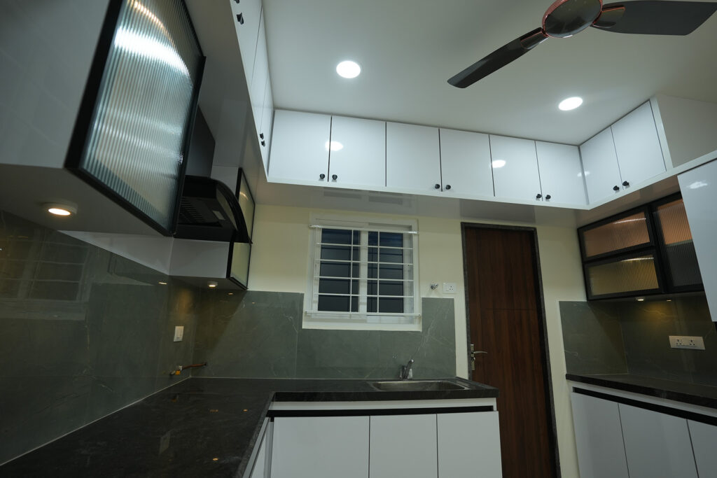 Kitchen interior with glass shutters, overhead cabinets and grey stone finish in Hyderabad
