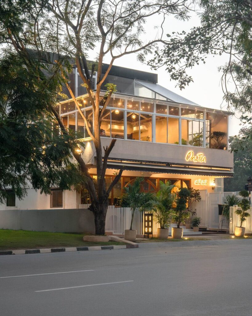 OneTen cafe exterior street view with illuminated facade and greenery by IWY Designs Hyderabad