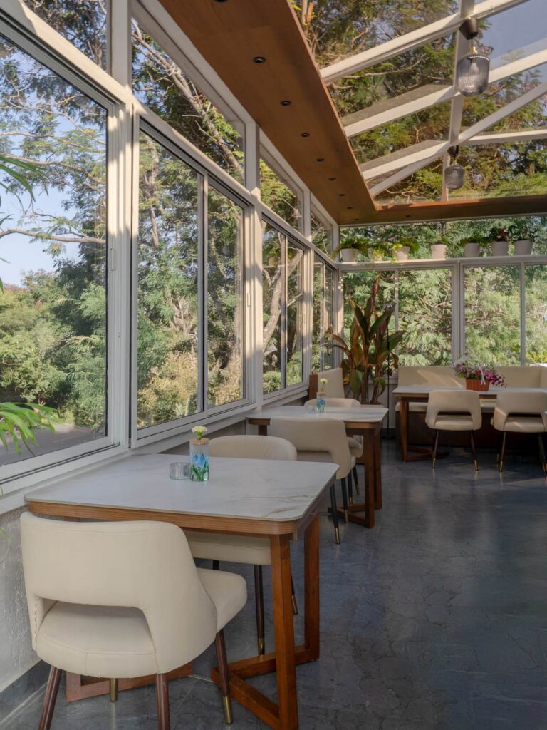 OneTen cafe glass dining area with natural light and greenery by IWY Designs Hyderabad