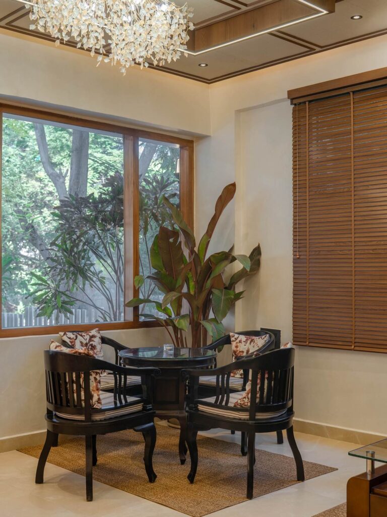 OneTen cafe window side seating corner with plants and warm finishes by IWY Designs Hyderabad